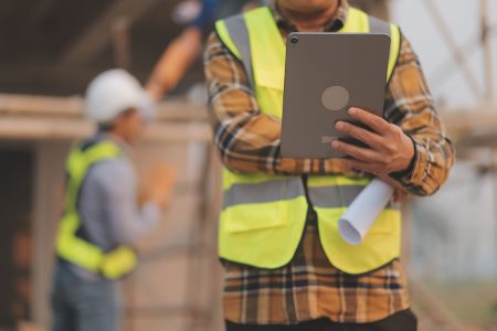 construction worker holding smart tablet and blueprints
